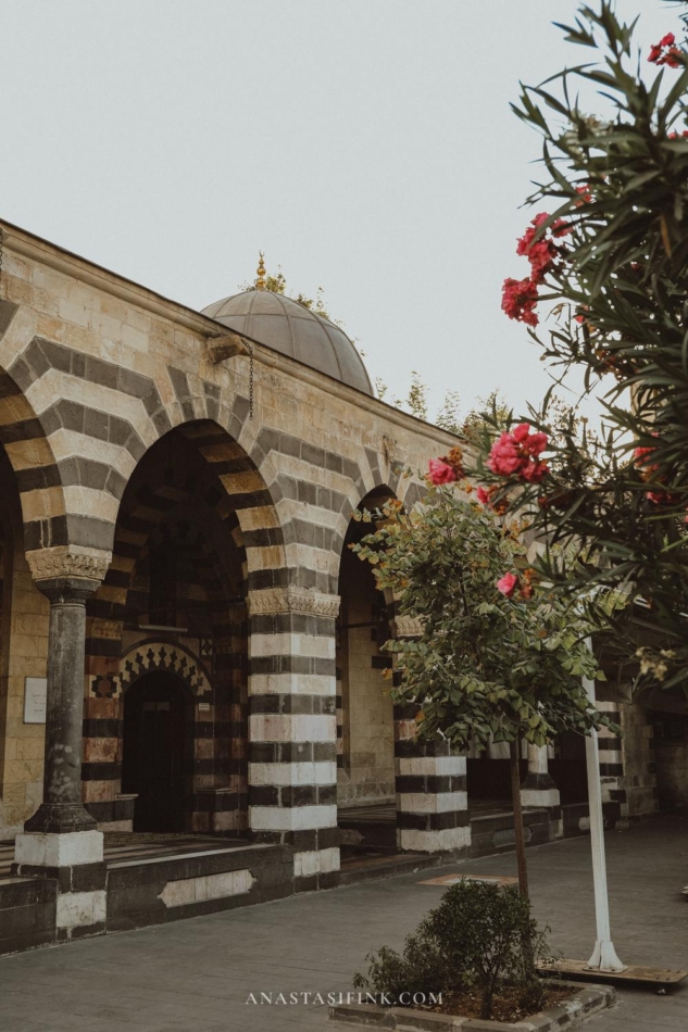 An archway in Gaziantep with striped stone patterns and flowering trees nearby.