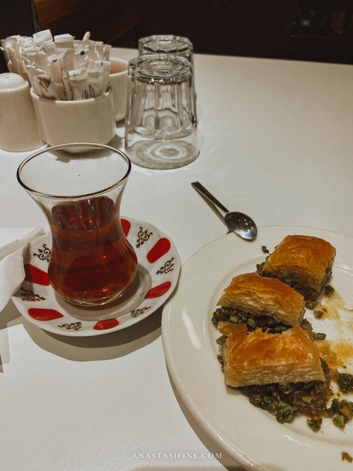 A plate with pieces of baklava and a traditional Turkish tea glass on a table.