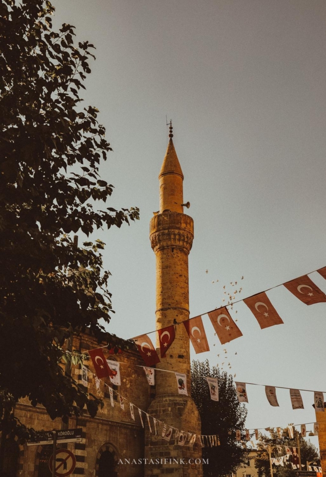 A minaret in Gaziantep with flags and banners hanging nearby, framed by the evening light.