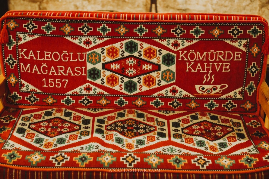 A colorful traditional rug with inscriptions in Kaleoğlu Mağarası Cafe.