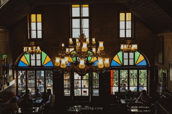 Chandeliers hanging from the ceiling inside Tahmis Kahvesi, with stained glass windows in the background.