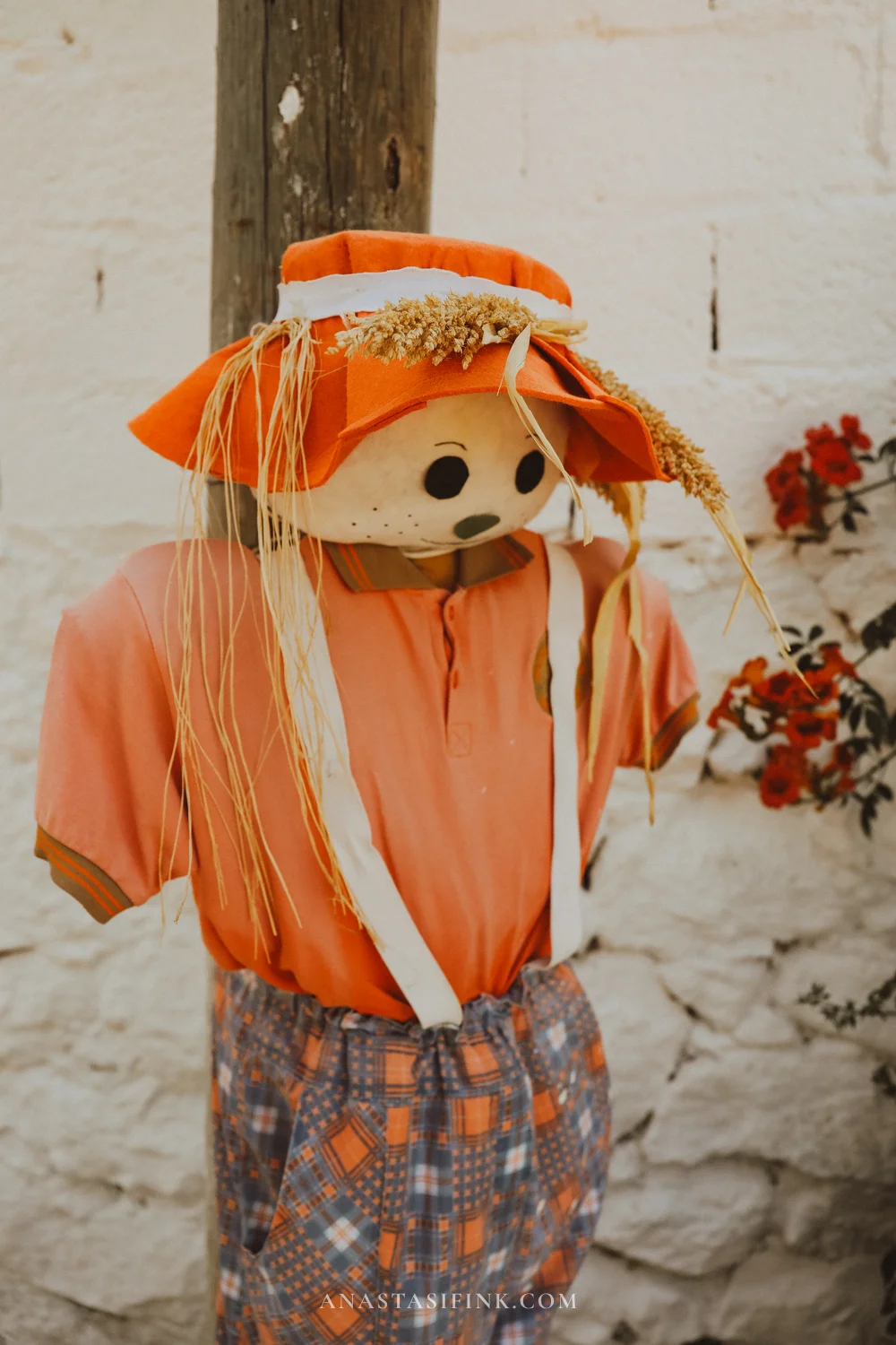 Scarecrow in an orange outfit by a stone wall