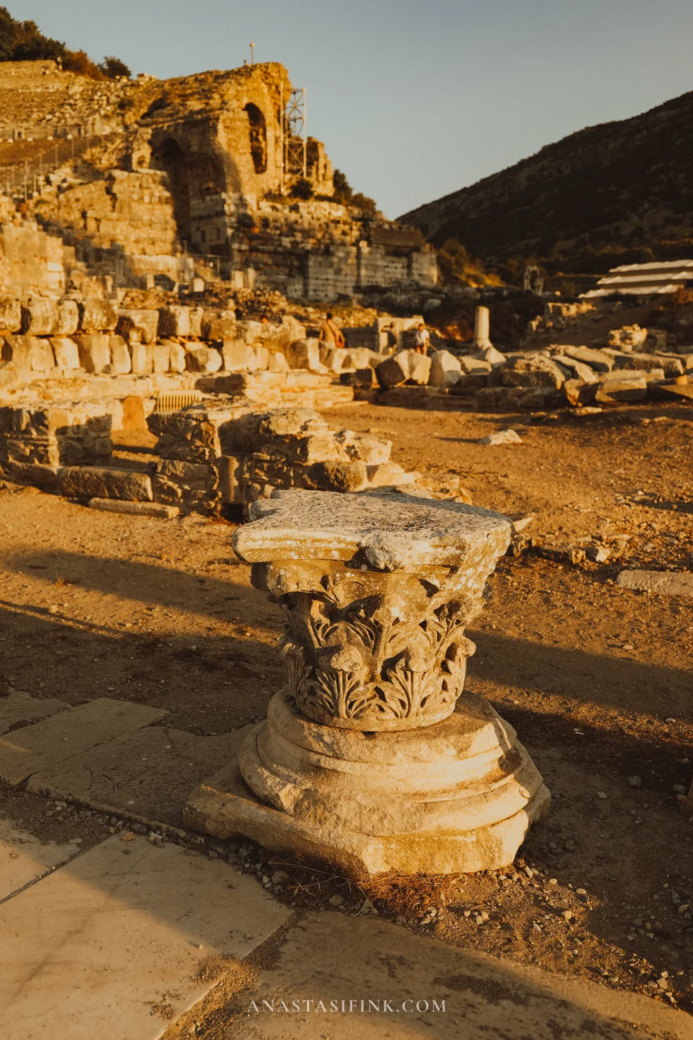 Corinthian capital against theatre ruins and a hill