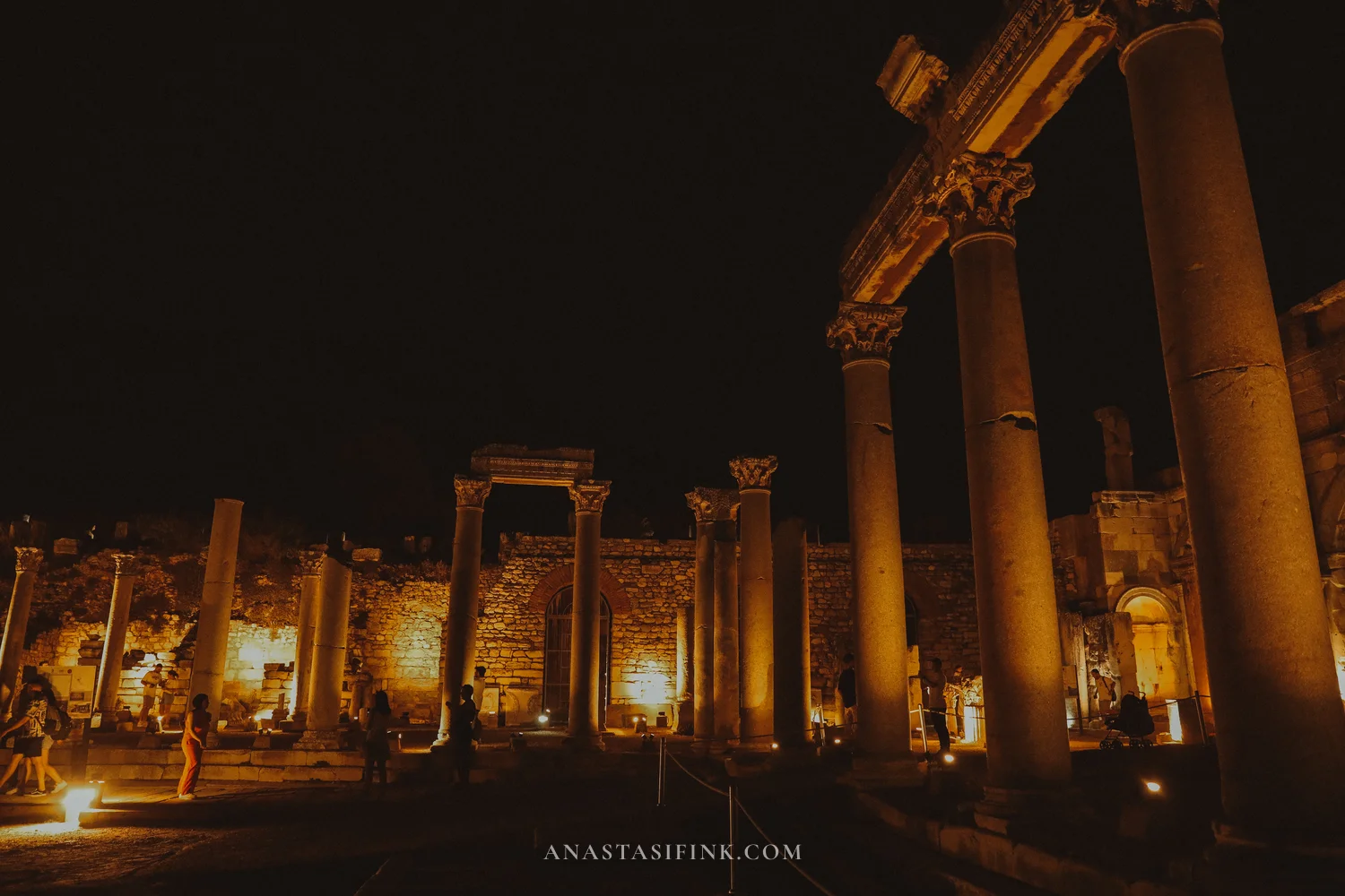 Wide view of the Lower Agora at night with a burning torch