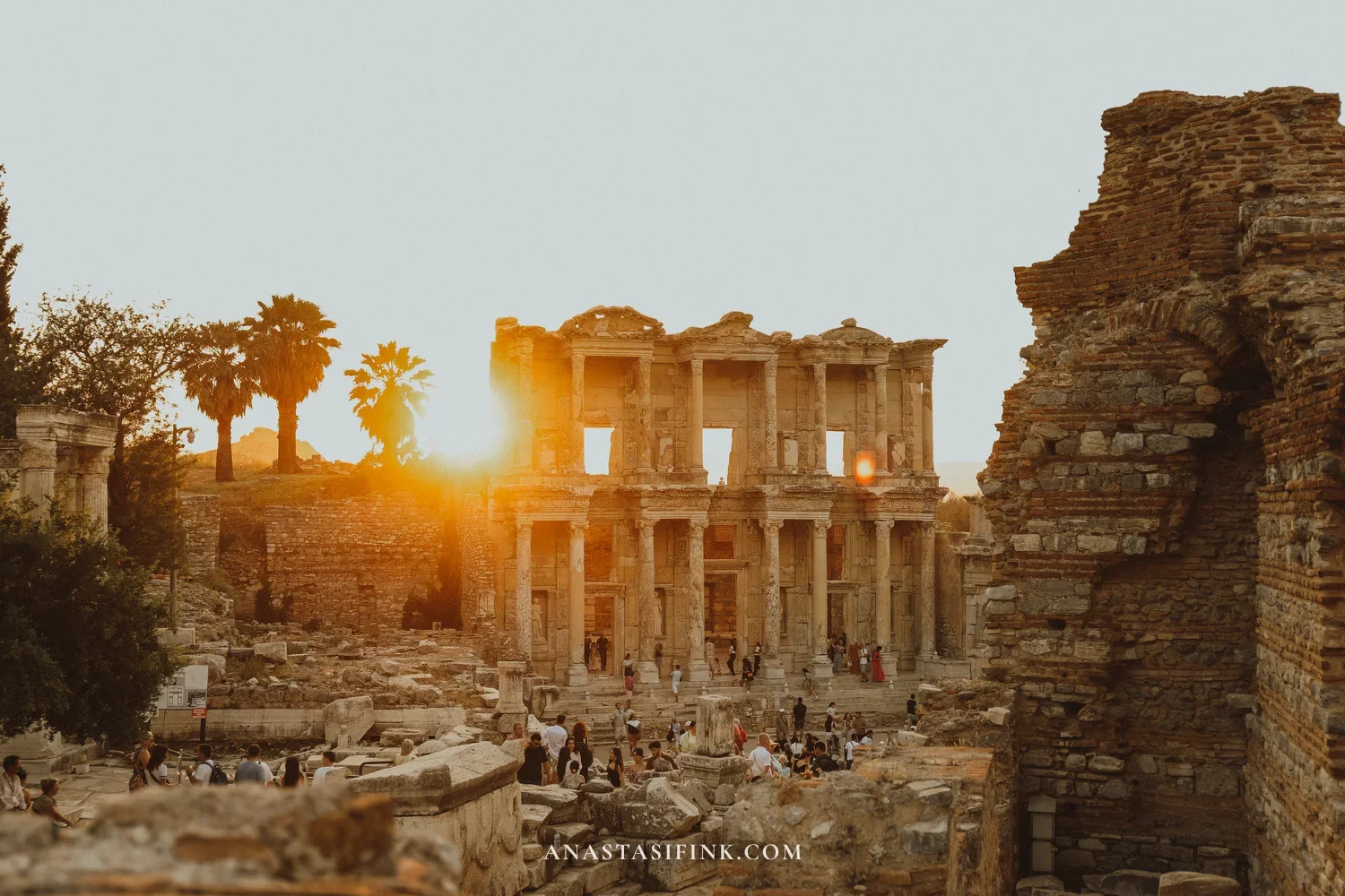 Library of Celsus at sunset — golden light, palm trees, silhouettes of people among the ruins