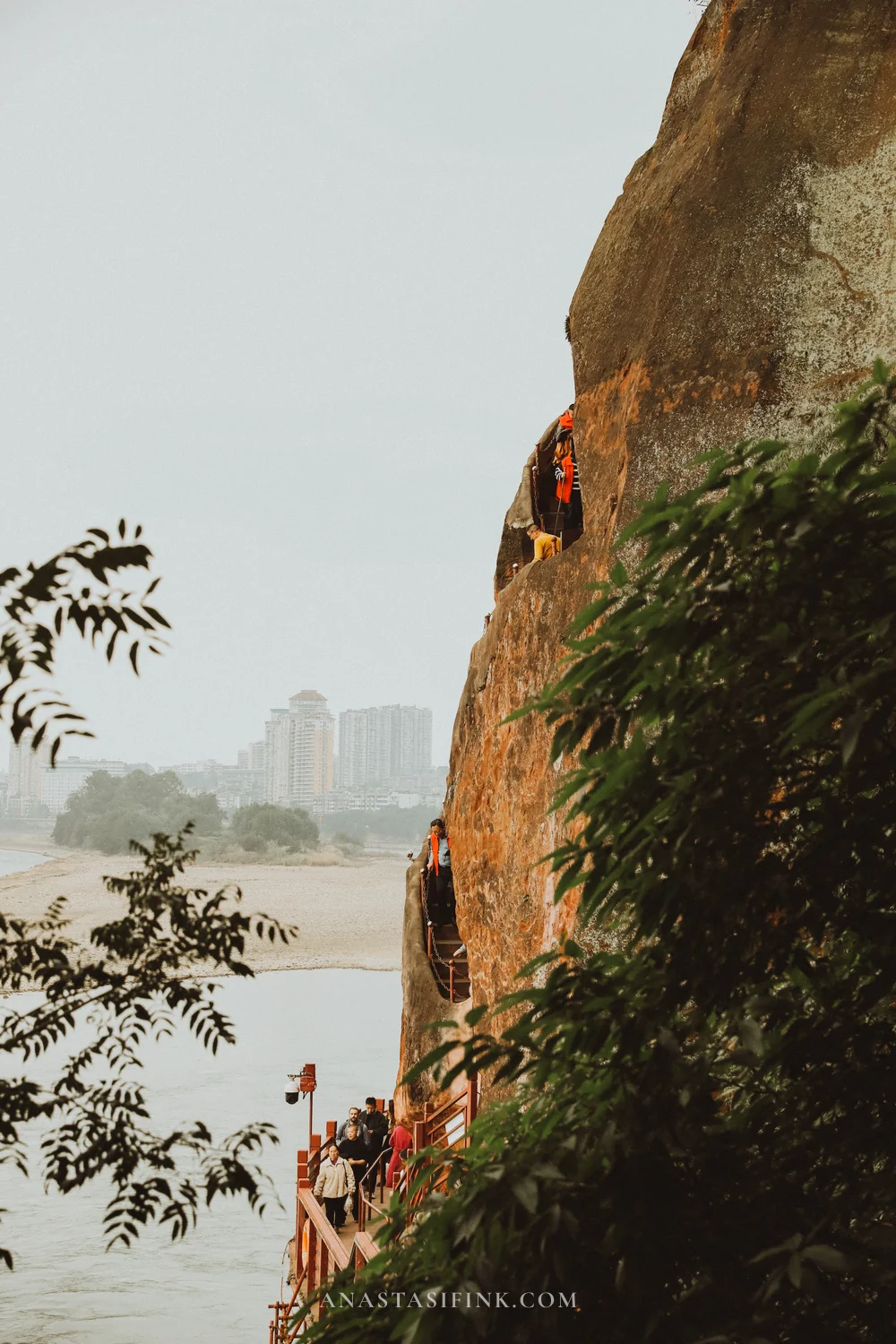 Path along the cliff with people and a view of the city across the river