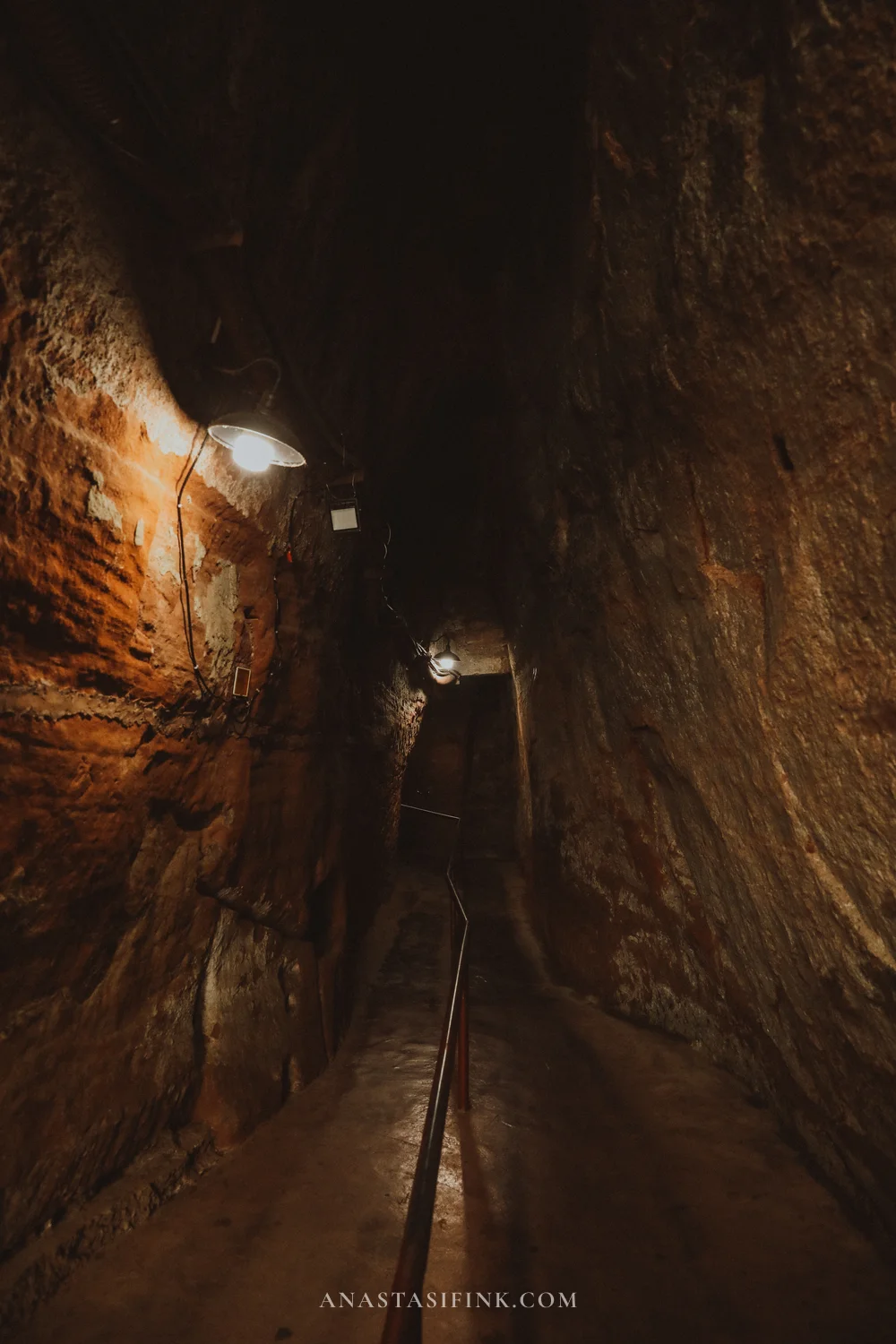 Narrow dark tunnel in the rock with a lamp on the descent