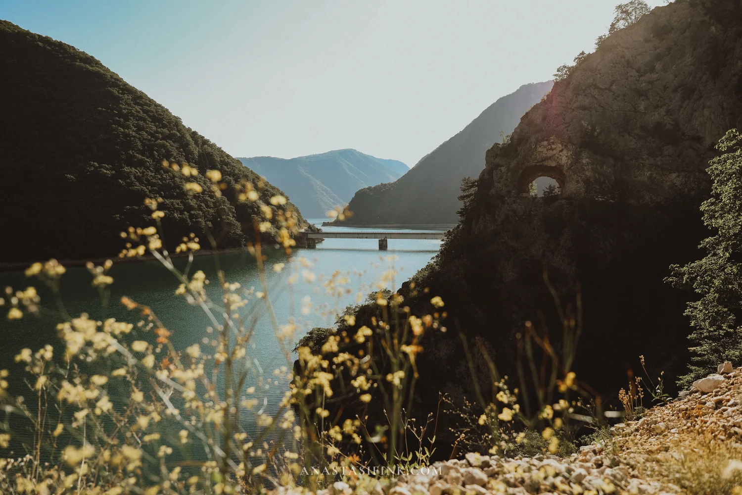 Piva Lake between steep green slopes with a bridge and rock tunnel, Montenegro