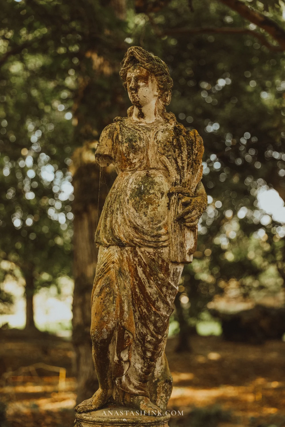 Weathered stone statue of a woman among trees in the Gijón Botanical Garden