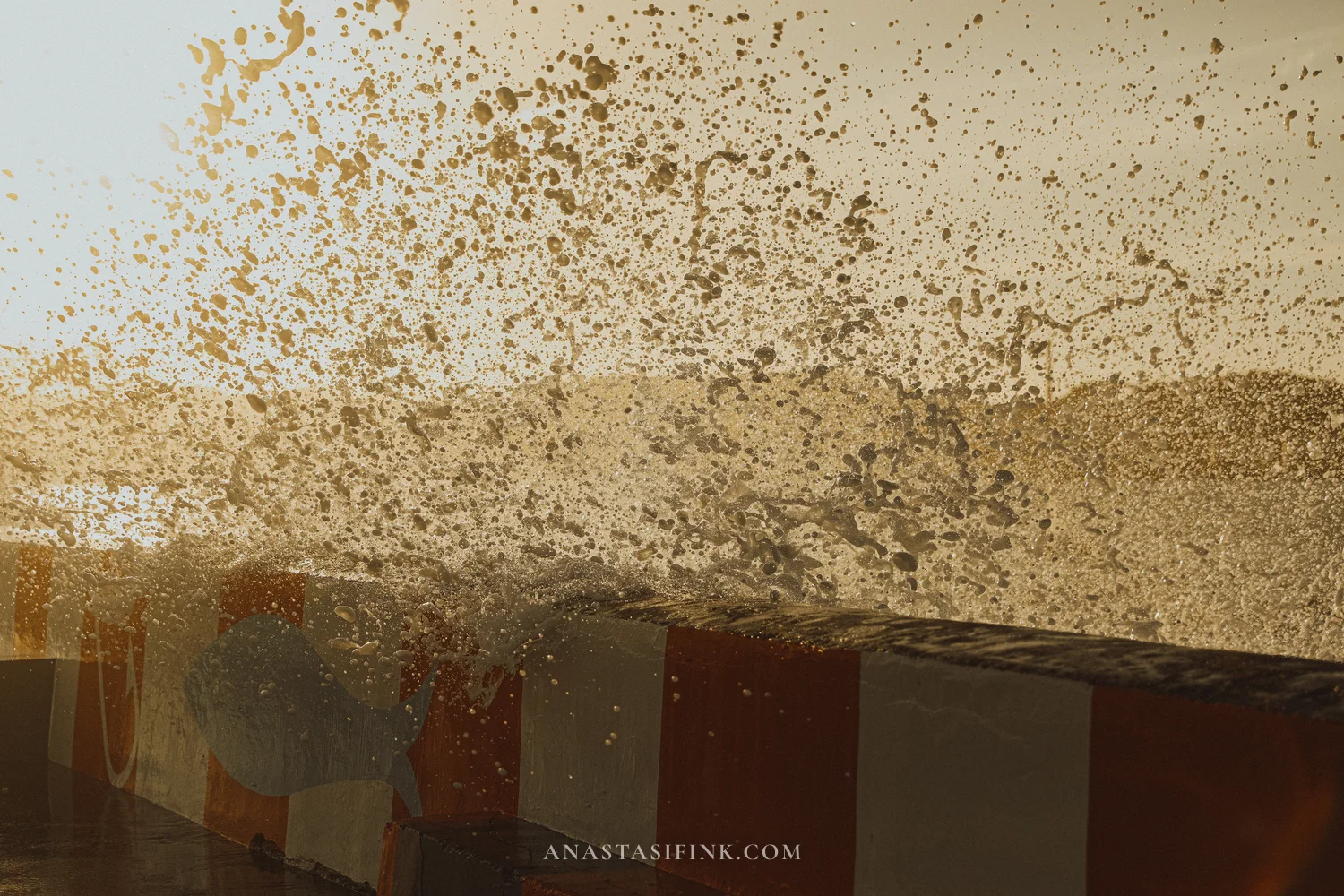 Close-up of sea spray flying over the striped breakwater wall in Gijón