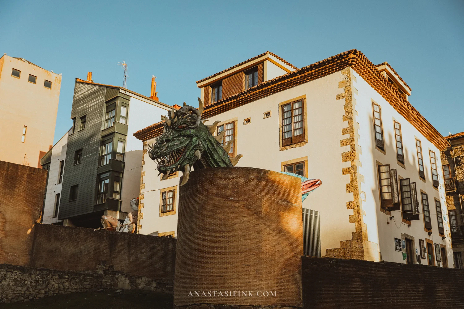 Dragon head sculpture above a brick wall next to a white house in Cimavilla, Gijón
