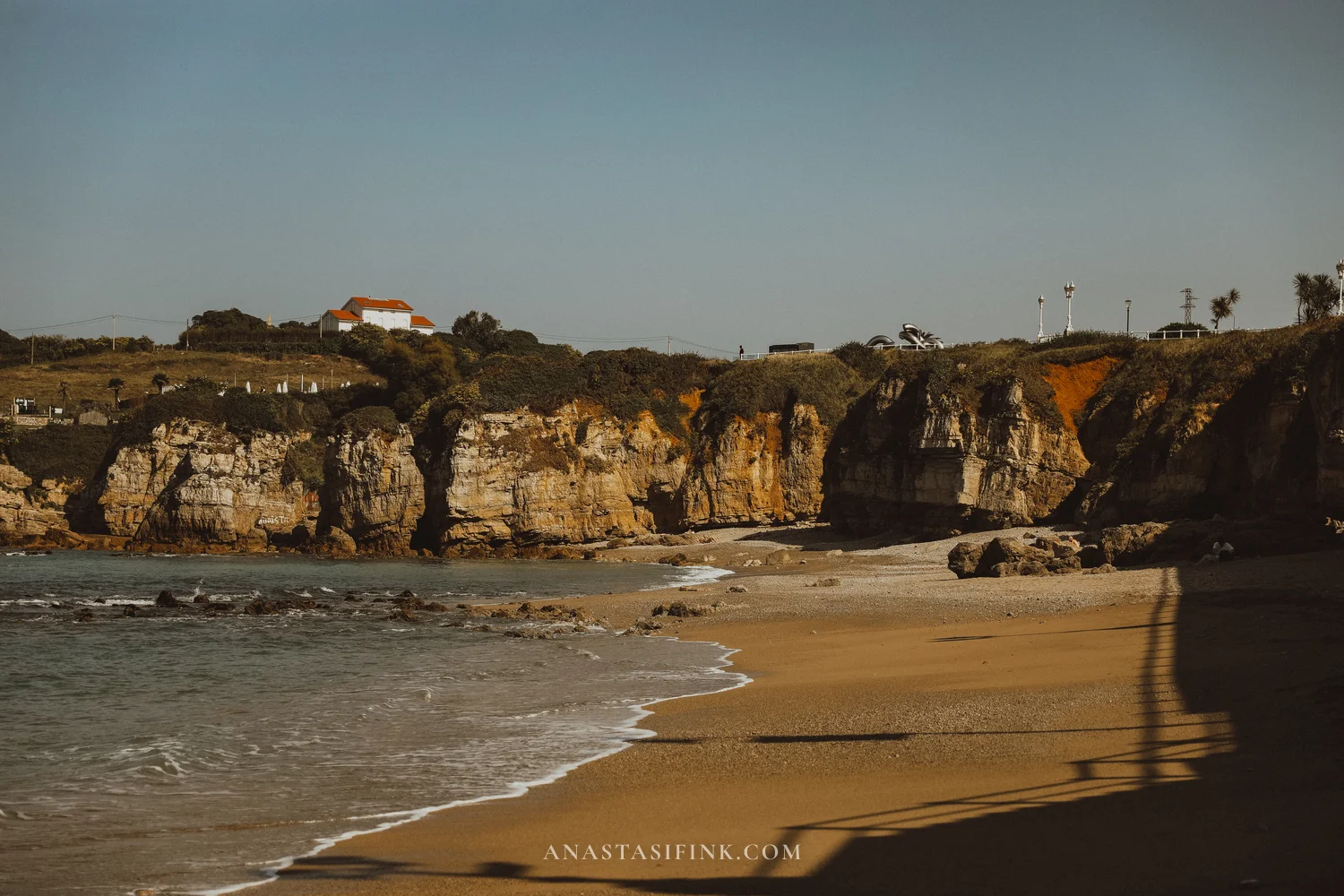 Sandy beach below limestone cliffs with a white house on top near the start of Senda del Cervigón in Gijón