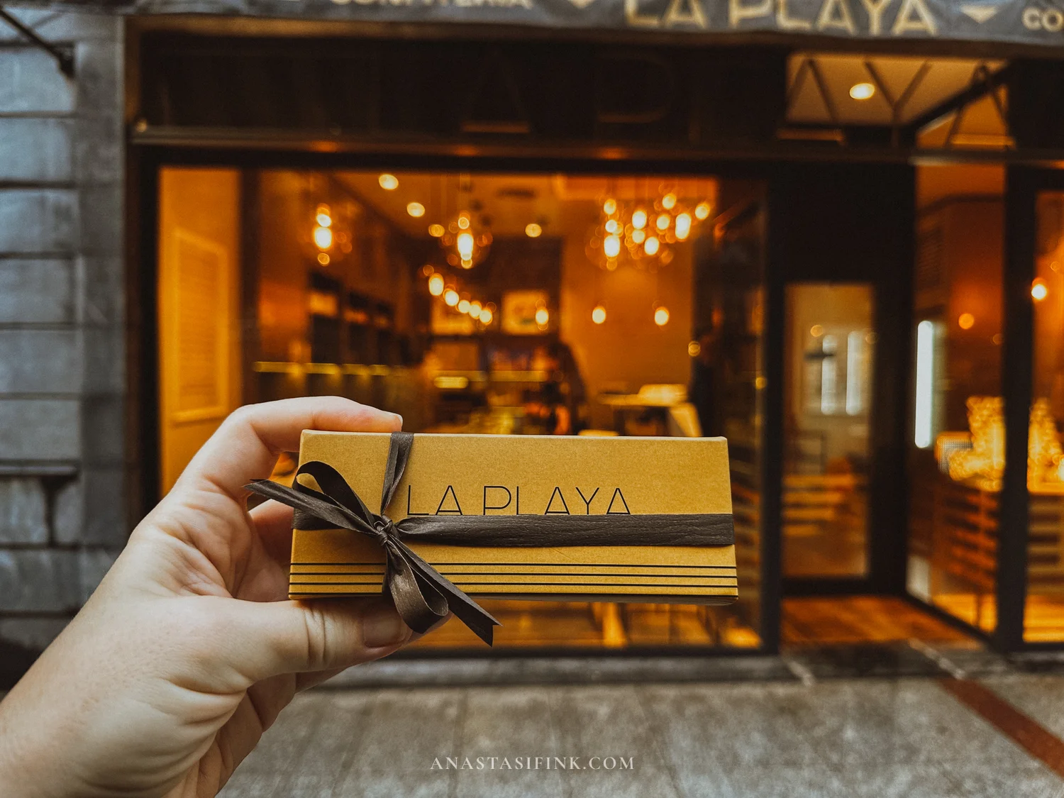 Gift box from Confitería La Playa held in front of the shop window in Gijón