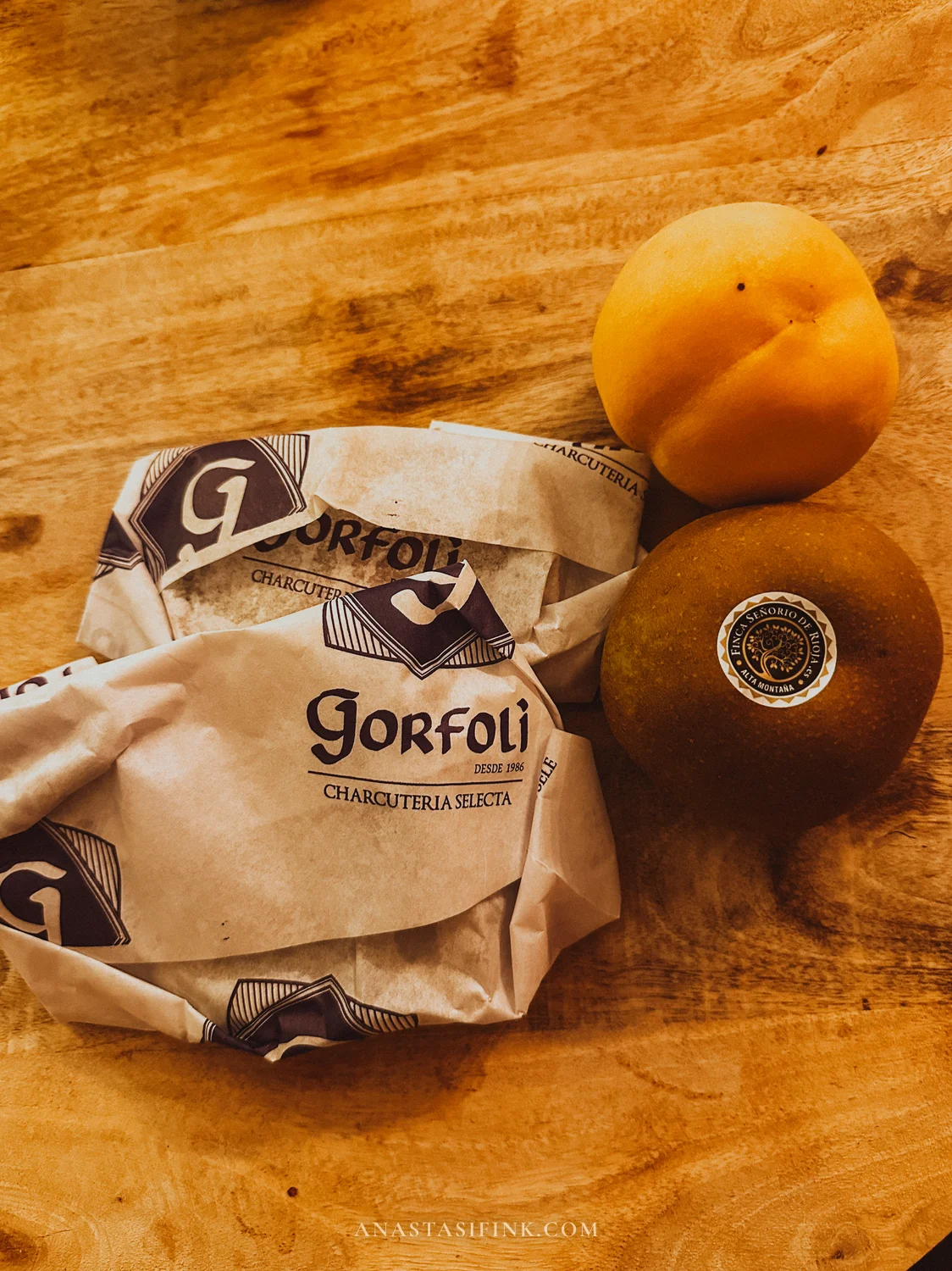 Paper-wrapped Cabrales cheese from Gorfolí charcuterie with a peach and an apple on a wooden table