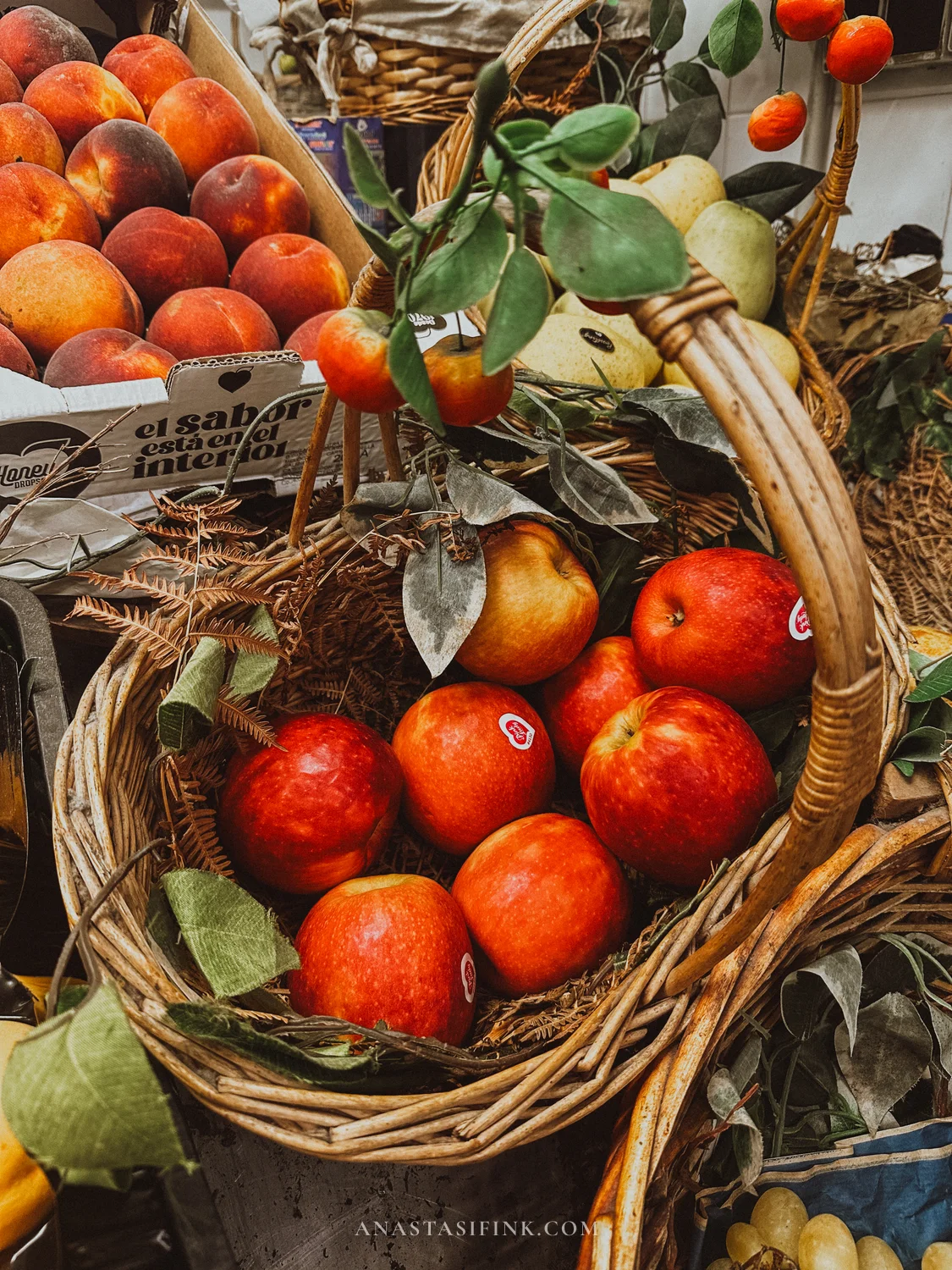 Basket of red apples and boxes of peaches at a fruit stall in Mercado del Sur, Gijón