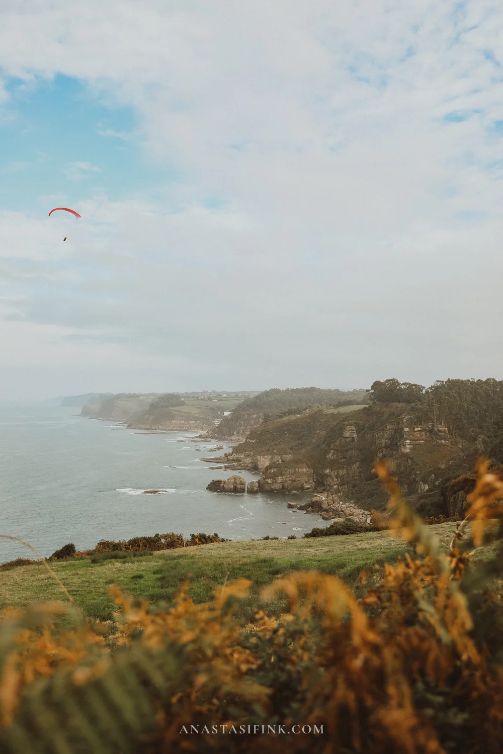 Red paraglider flying over the cliffs of Colina del Cuervo near Gijón