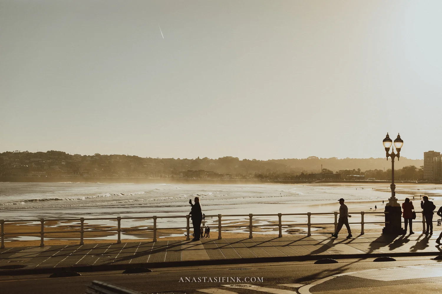 San Lorenzo beach promenade in Gijón with people walking and waves in the morning