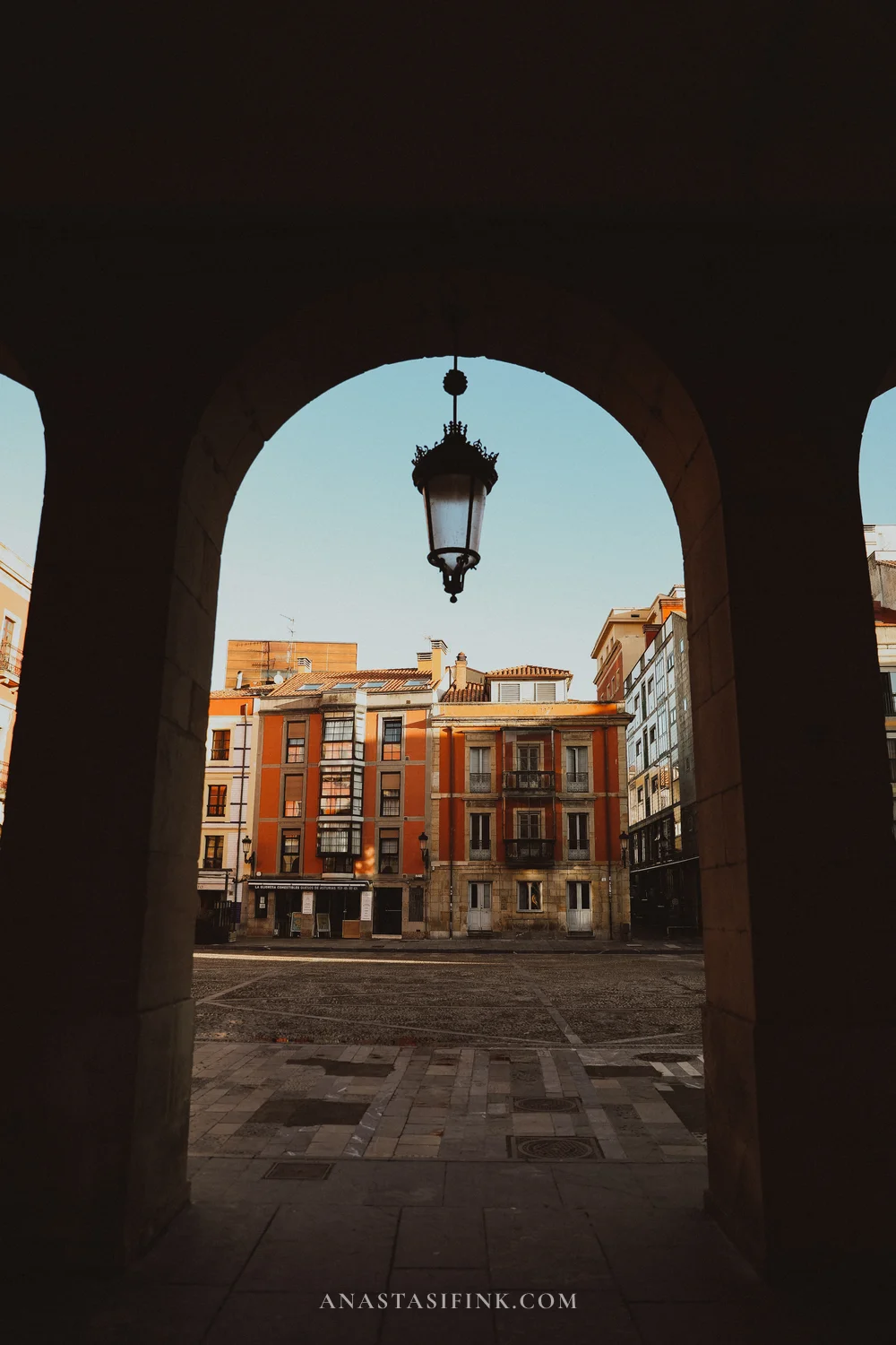 Arcade of Plaza Mayor in Gijón with an iron lantern and orange facades in morning light