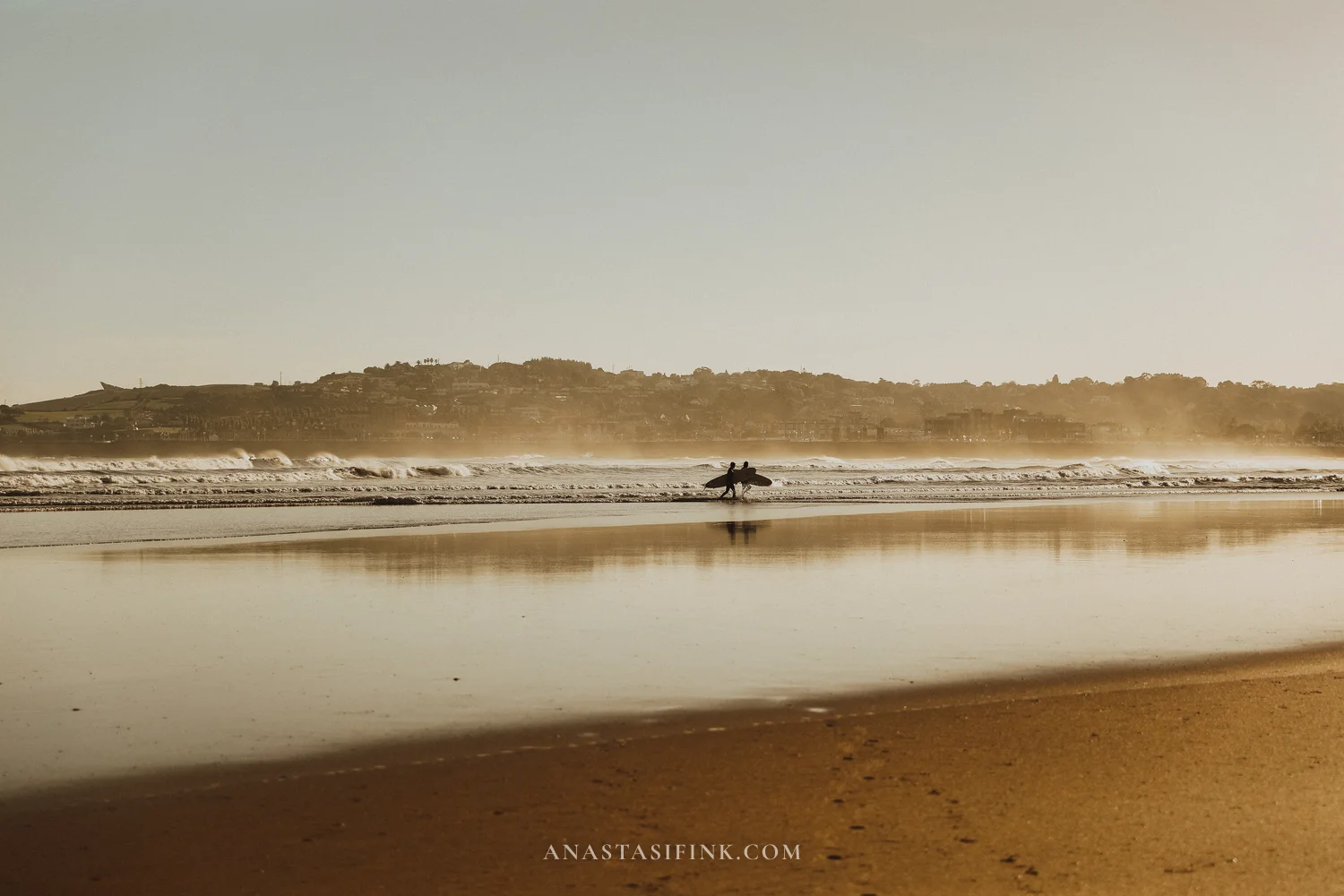 Two surfers walking into the waves on San Lorenzo beach in Gijón in the morning